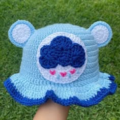 a crocheted blue bear hat on someone's hand with grass in the background