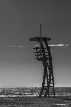 a tall wooden structure sitting on top of a sandy beach next to the ocean under a cloudy sky