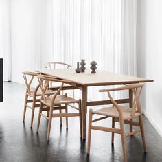 a wooden table with chairs around it in front of a white curtained room window