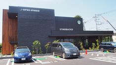 two cars are parked in front of a starbucks building that is black and has the starbucks logo on it