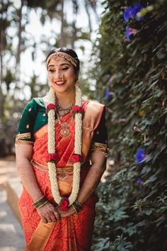 a woman in an orange and green sari with flowers around her neck smiling at the camera