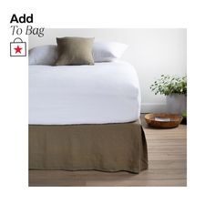 a bed with white sheets and pillows in a room next to a plant on the floor