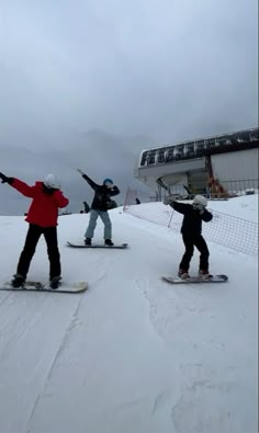 three snowboarders are standing in the snow on their boards and one is holding his arms up