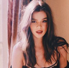 a woman with long hair wearing a black dress and posing for a photo in front of a window