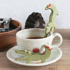 there is a cup with some tea in it and a small toy dinosaur on the saucer