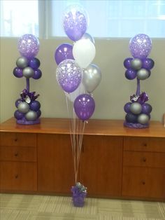 purple and silver balloons are on display in front of a wooden dresser with drawers,