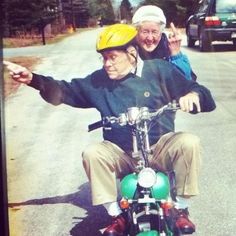 an older man riding on the back of a green motorcycle next to another old man