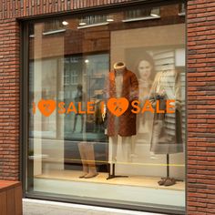 a store front window with mannequins in the window and an orange sale sign