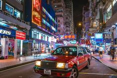 a red car parked on the side of a street next to tall buildings at night