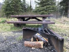 a fire pit in the middle of a forest with a bench and logs on it