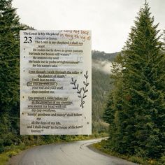 a sign on the side of a road with trees and mountains in the back ground