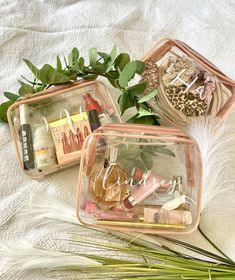 three clear containers with personal items in them on a white cloth covered surface, one is filled with leaves and the other contains cosmetics