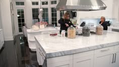 two women in a kitchen preparing food on a counter top with an oven hood over the stove