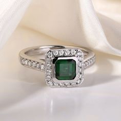 an emerald and diamond ring sitting on top of a white cloth