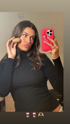 a woman taking a selfie with her cell phone in front of her face and wearing a black turtle neck top