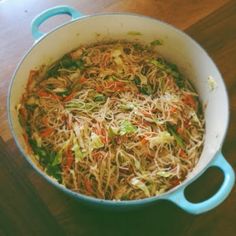 a pot filled with noodles and vegetables on top of a wooden table