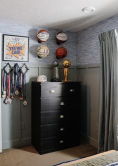 a black dresser in a bedroom with basketballs on the wall and medals hanging above it