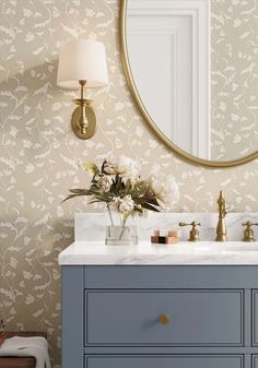 a bathroom vanity with two sinks and a round mirror above it, in front of a floral wallpaper