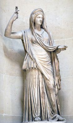 the statue is holding a bottle in one hand and an object in the other, with words describing hera