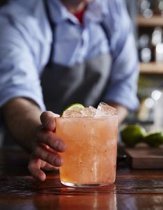 a person holding a drink in their hand on a bar with limes around it