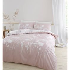 a pink bed with white flowers on the comforter and pillow cases in front of a window