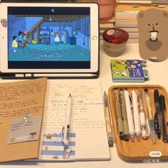 an ipad and some writing supplies on a desk with a teddy bear in the background