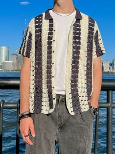 a man standing in front of the water wearing a crocheted shirt and hat