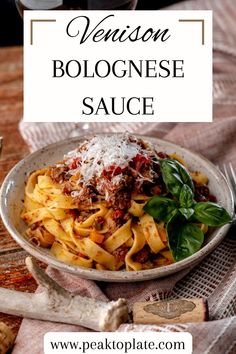 a white plate topped with pasta covered in meat and sauce next to a glass of wine