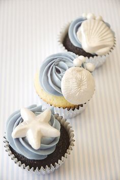 three cupcakes with blue frosting and seashell decorations on the top one