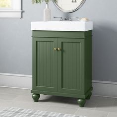 a green cabinet with a white sink in the corner and a round mirror above it