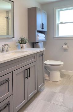 a white toilet sitting next to a sink in a bathroom under a window with a towel dispenser on it