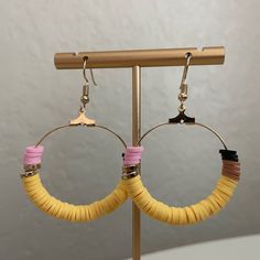 two pairs of yellow and pink hoop earrings on a metal stand against a white wall