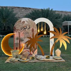 a table set up with palm trees, plates and cups on it in front of a large sign