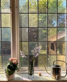 two vases filled with flowers sitting on top of a window sill next to a watering can