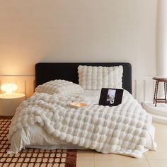 a bed with white blankets and pillows on top of it next to a night stand