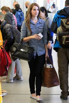 a woman is walking through an airport with her hand on her purse and other people in the background