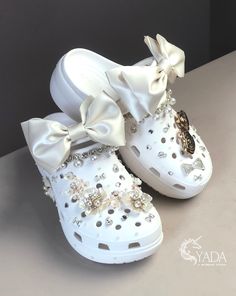 a pair of white shoes with bows and pearls on the side, sitting on a table