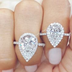 two pear shaped diamond engagement rings on top of each other's fingers in front of the camera