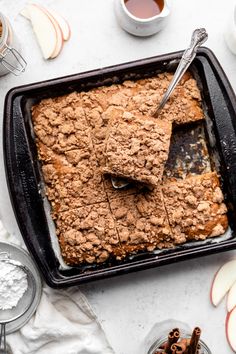 an apple crumble cake in a baking pan with spoons and apples around it