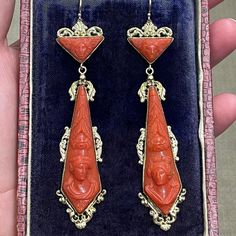 Here's a spectacular pair of large antique coral earrings. The colour of the cameos is a rich reddish orange.  I love the strong geometry of the triangular tops above the kite-shaped drops.  Earring styles of the late 1830s and 1840s favoured long, flat jewels like these. They're relatively two-dimensional compared with the rounded, plumper shapes of the mid-Victorian period.  Coral was the height of fashion. Its fragile nature means these are rare survivors. A man and woman face each other, as Earring Styles, Reddish Orange, Coral Earrings, Natural Coral, Antique Boxes, Coral Jewelry, Yellow Gold Setting, Woman Face, Designer Earrings