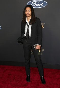 a man in a suit and tie on the red carpet at an awards event,