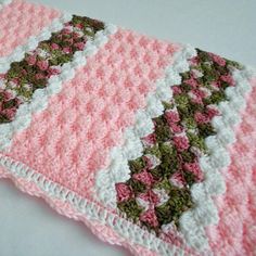 a pink and white crocheted blanket laying on top of a table