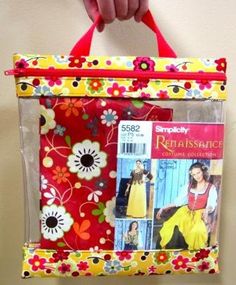 a hand holding a red and yellow bag with pictures on it's front pocket