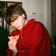 two young men eating food in front of a microwave oven and refrigerator freezer door