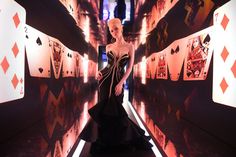 a woman in a black dress walking down a hallway with playing cards on the walls