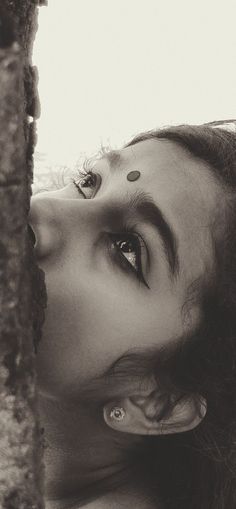 black and white photograph of a woman's face peeking out from behind a tree