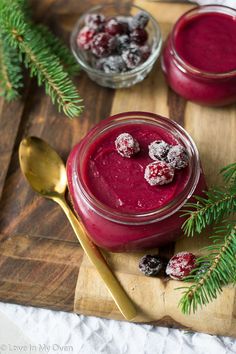 two small jars filled with red liquid and topped with cranberries on a cutting board