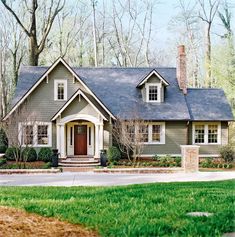 a gray house with white trim and windows in the middle of a green yard, surrounded by trees