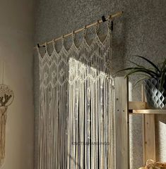 a room with a shelf, plant and window curtain in front of the window that has a macrame hanging on it