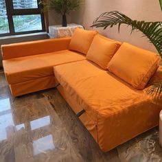 an orange couch sitting on top of a hard wood floor next to a potted plant